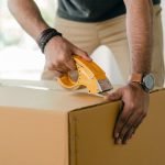crop man taping carrying box with scotch